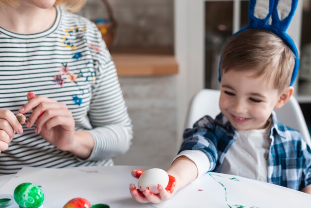 Netter kleiner Junge mit Hasenohren, die ein Ei halten