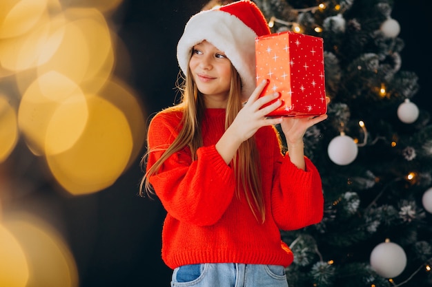 Netter Mädchenjugendlicher im roten Weihnachtsmannhut durch Weihnachtsbaum