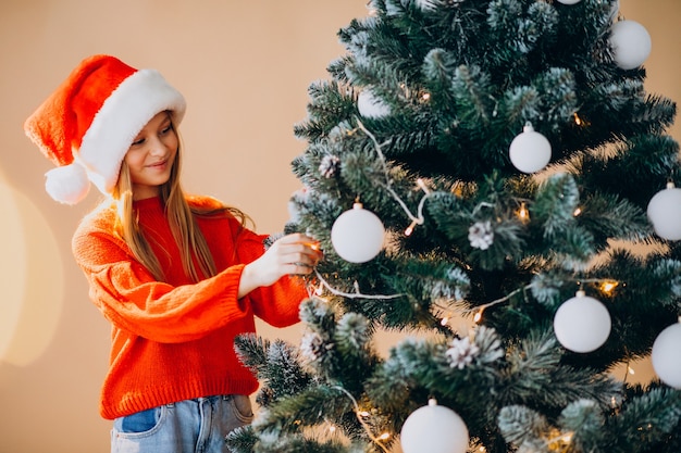 Netter Mädchenjugendlicher im roten Weihnachtsmannhut durch Weihnachtsbaum
