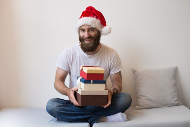 Netter Mann, der Sankt-Hut trägt und Geschenkboxen auf Couch hält