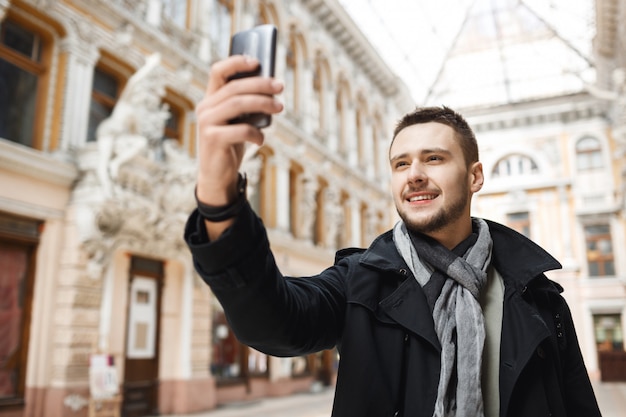 Kostenloses Foto netter mann, der selfie nimmt, während er durch schöne stadt geht.