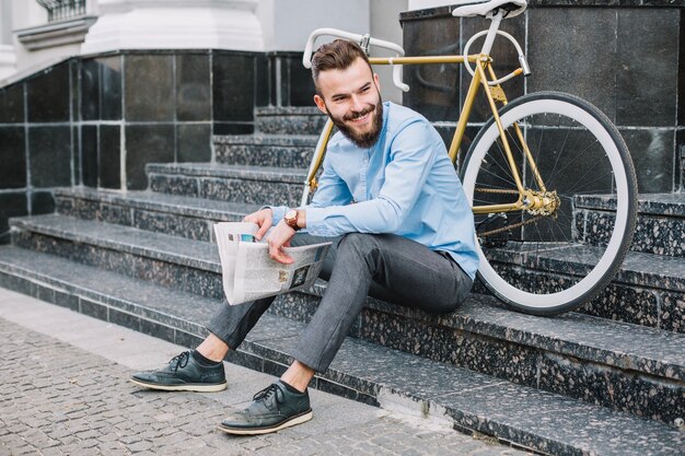 Netter Mann mit der Zeitung, die auf Treppe sitzt