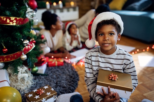 Netter schwarzer Junge mit Geschenkbox am Weihnachtstag zu Hause