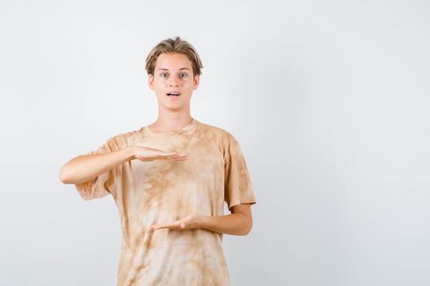 Netter Teenager, der ein Größenschild im T-Shirt zeigt und sich wundert, Vorderansicht.