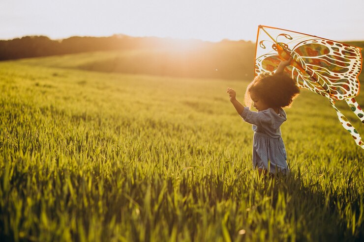Kostenlose Foto nettes afrikanisches babymädchen auf dem feld auf dem sonnenuntergang, der mit drachen spielt