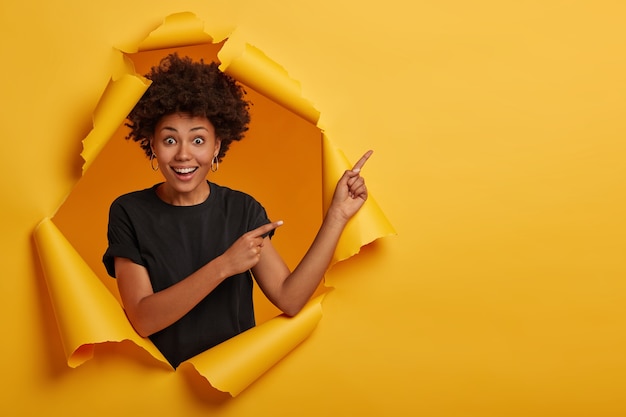 Nettes attraktives weibliches Model mit knackigen Haarspitzen beiseite, zeigt Werbung, fühlt sich fröhlich und neugierig an