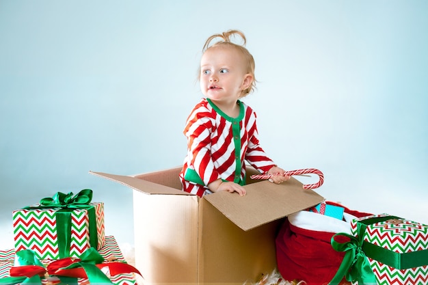 Nettes Baby 1 Jahr alt, das im Kasten über Weihnachtshintergrund sitzt. Urlaub, Feier, Kinderkonzept