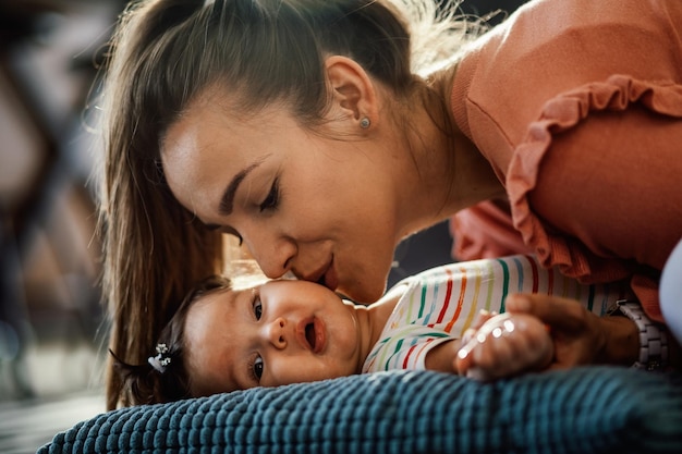 Nettes Babymädchen, das auf dem Kissen liegt, während es von ihrer Mutter geküsst wird