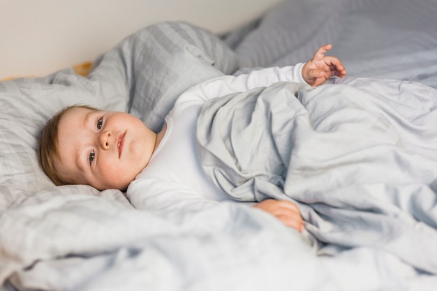 Nettes blondes Baby im weißen Bett mit Decken