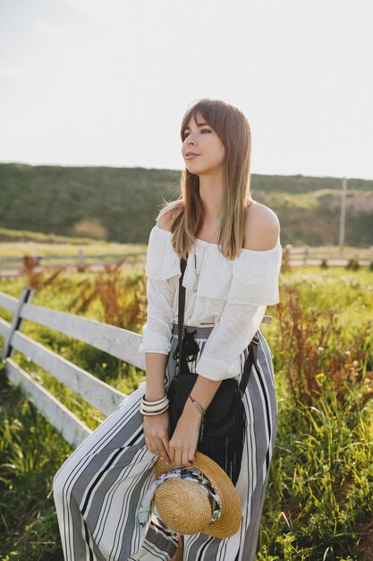 Nettes hübsches sonniges Porträt der lächelnden jungen schönen stilvollen Frau, Frühlingssommer-Modetrend, Boho-Art, Strohhut, Landschaftswochenende, sonniger, schwarzer Geldbeutel