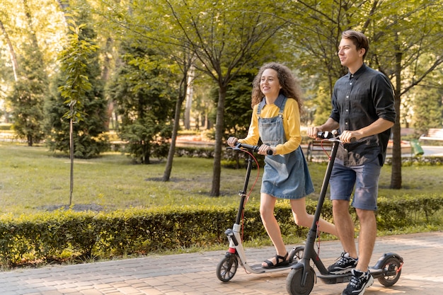 Nettes junges Paar, das Roller draußen reitet