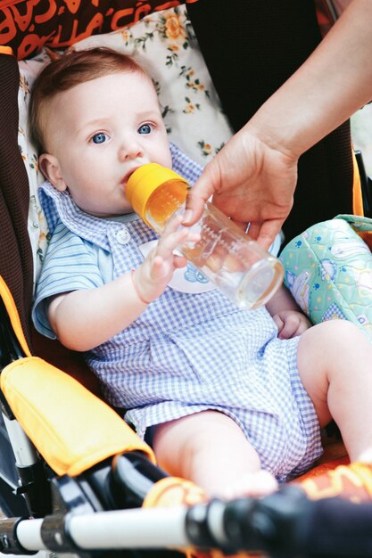 Nettes kleines Baby der blauen Augen mit Flasche im Spaziergänger