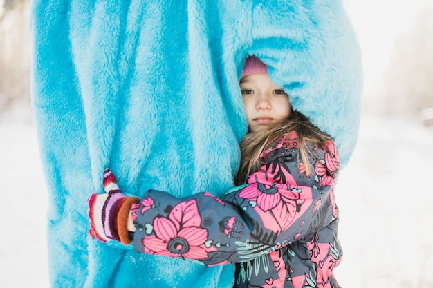 Nettes kleines Mädchen, das eine Person in einem flauschigen blauen Kostüm umarmt