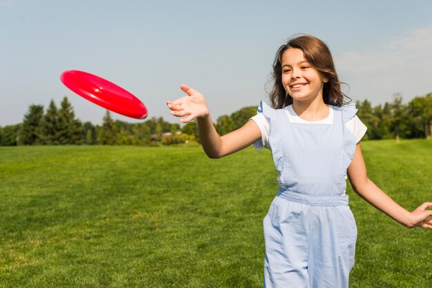 Nettes kleines Mädchen, das mit rotem Frisbee spielt