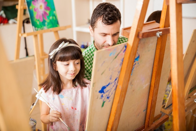 Nettes kleines Mädchen, das während des Kunstunterrichts in der Schule Hilfe von ihrem Lehrer bekommt