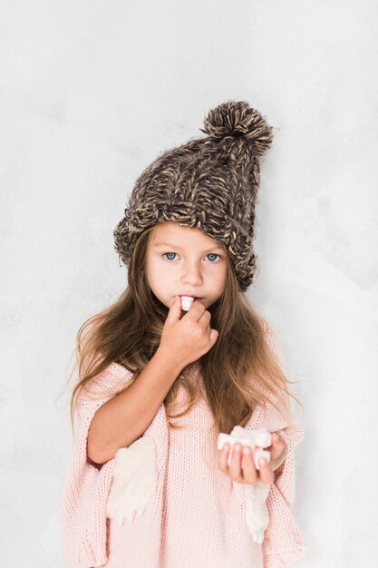 Nettes kleines Mädchen, das Winterhut isst und trägt