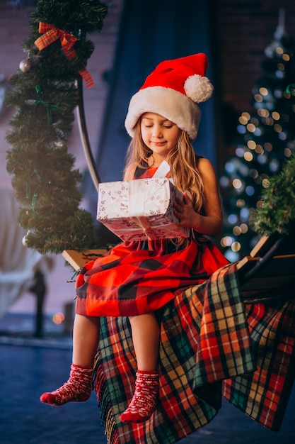 Nettes kleines Mädchen im Sankt-Hut, der Weihnachtsgeschenk auspackt