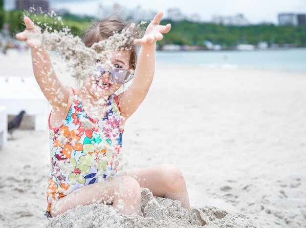 Nettes kleines Mädchen in der Sonnenbrille spielt mit Meersand am Strand.