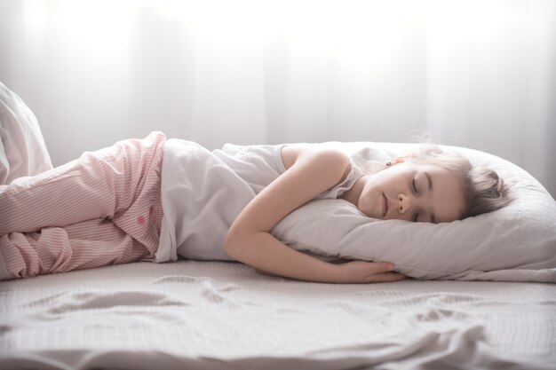 Nettes kleines Mädchen schläft süß in einem weißen gemütlichen Bett, das Konzept der Kinderruhe und des Schlafes