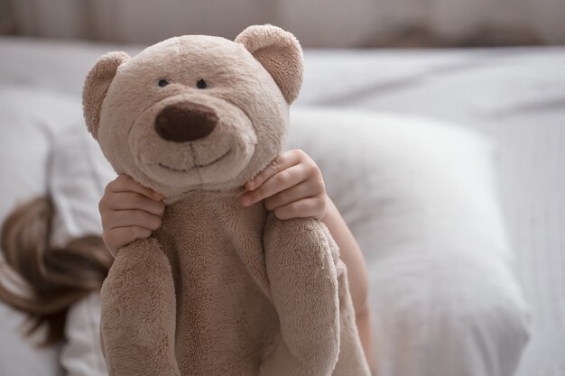 Nettes kleines Mädchen schläft süß in einem weißen gemütlichen Bett mit einem weichen Bärenspielzeug, dem Konzept der Kinderruhe und des Schlafes