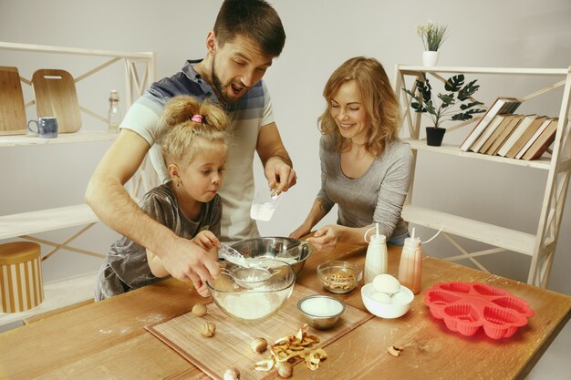 Nettes kleines Mädchen und ihre schönen Eltern bereiten den Teig für den Kuchen in der Küche zu Hause vor. Familienlebensstilkonzept