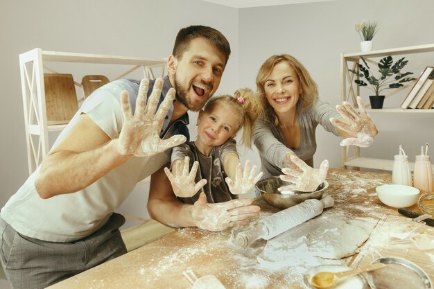 Nettes kleines Mädchen und ihre schönen Eltern bereiten den Teig für den Kuchen in der Küche zu Hause vor. Familienlebensstilkonzept