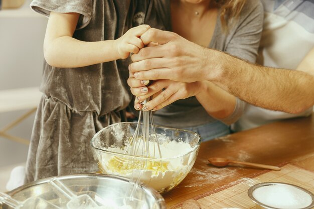 Nettes kleines Mädchen und ihre schönen Eltern bereiten den Teig für den Kuchen in der Küche zu Hause vor. Familienlebensstilkonzept