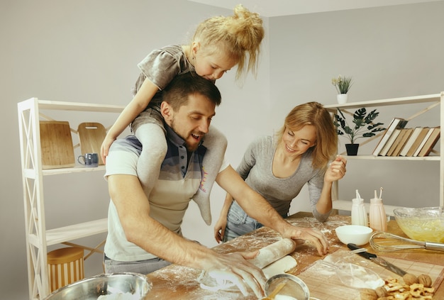 Nettes kleines Mädchen und ihre schönen Eltern bereiten den Teig für den Kuchen in der Küche zu Hause vor. Familienlebensstilkonzept