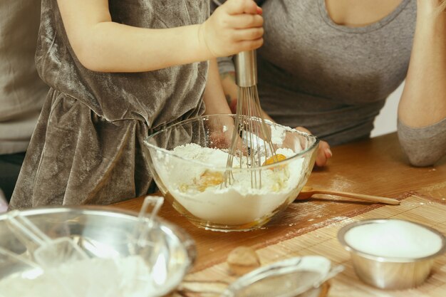 Nettes kleines Mädchen und ihre schönen Eltern bereiten den Teig für den Kuchen in der Küche zu Hause vor