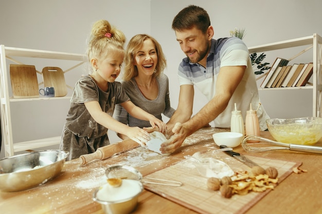 Nettes kleines Mädchen und ihre schönen Eltern bereiten den Teig für den Kuchen in der Küche zu Hause vor