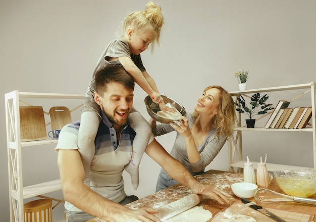 Kostenloses Foto nettes kleines mädchen und ihre schönen eltern bereiten den teig für den kuchen in der küche zu hause vor.