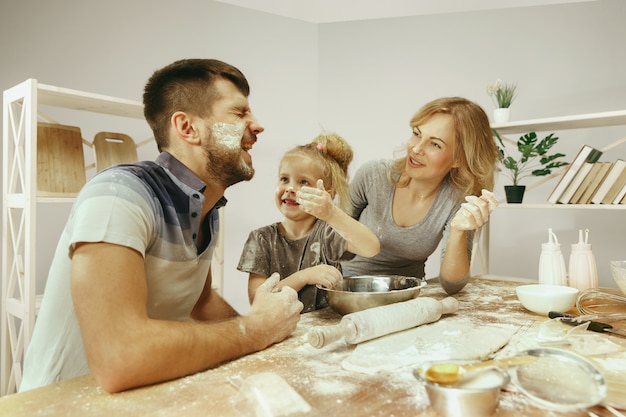 Kostenloses Foto nettes kleines mädchen und ihre schönen eltern bereiten den teig für den kuchen in der küche zu hause vor