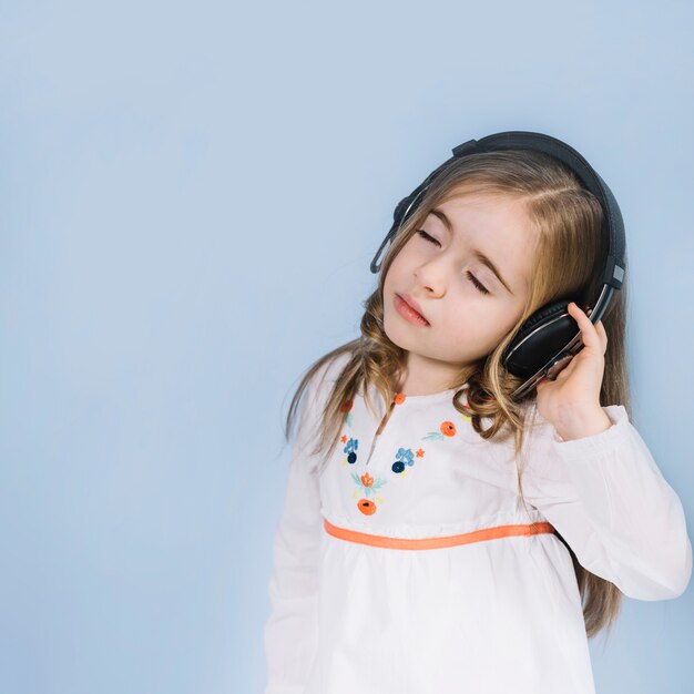 Nettes kleines Mädchen, welches die Musik auf Kopfhörer gegen blauen Hintergrund genießt