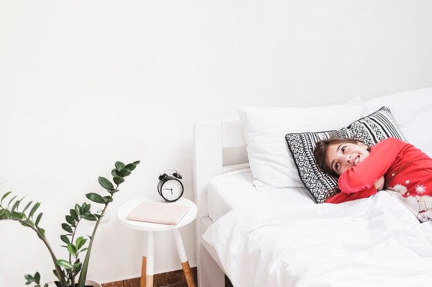 Nettes lächelndes Mädchen, das auf Bett im Schlafzimmer liegt