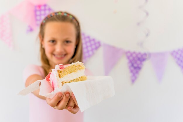 Nettes lächelndes Mädchen, das Kuchenscheibe am Geburtstagsteil gibt