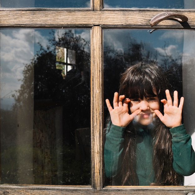 Kostenloses Foto nettes mädchen, das durch glasfenster schaut