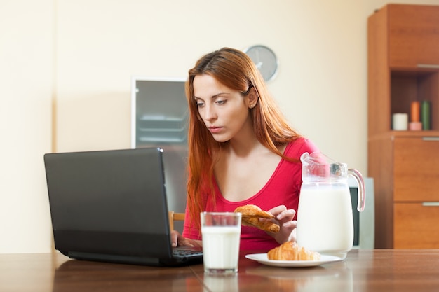 Nettes Mädchen, das E-Mail im Laptop während der Frühstückzeit zu Hause überprüft