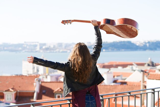 Nettes Mädchen, das Gitarre über Kopf auf Dachspitze hält