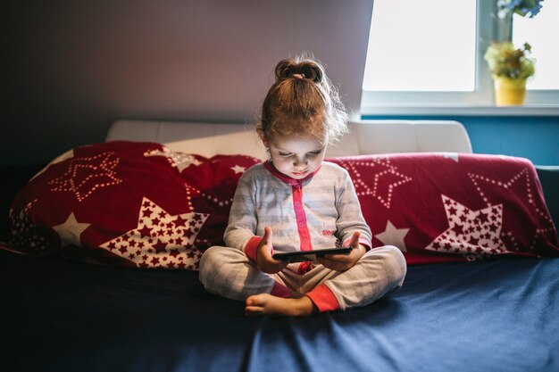 Nettes Mädchen, das Smartphone auf Bett verwendet