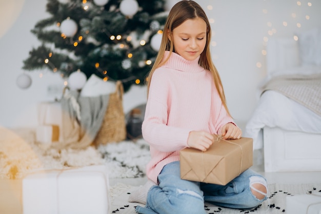 Nettes Mädchen, das Weihnachtsgeschenke durch Weihnachtsbaum hält