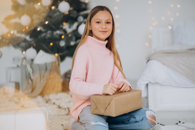 Nettes Mädchen, das Weihnachtsgeschenke durch Weihnachtsbaum hält