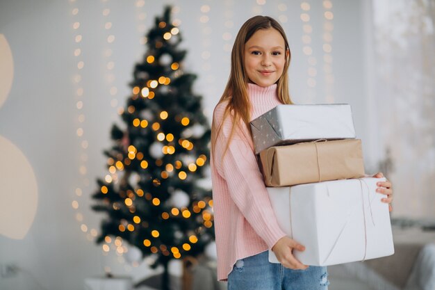 Nettes Mädchen, das Weihnachtsgeschenke durch Weihnachtsbaum hält