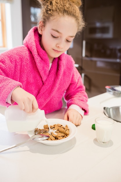 Kostenloses Foto nettes mädchen gießt milch in cornflakes in der küche