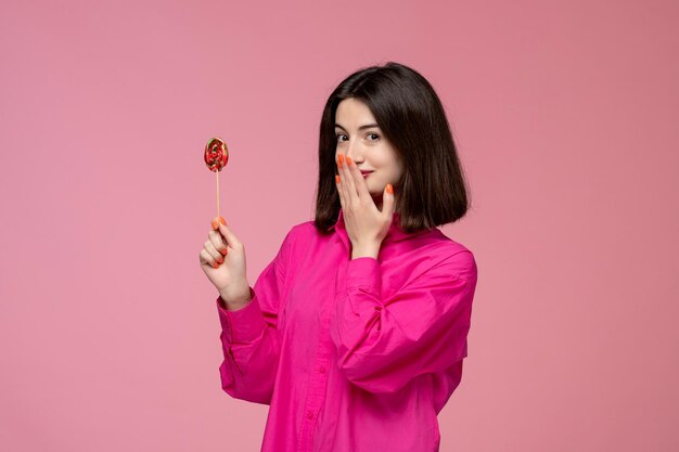 Nettes Mädchen hübsches junges schönes Brunettemädchen im rosafarbenen Hemd, das Mund mit Lutscher bedeckt