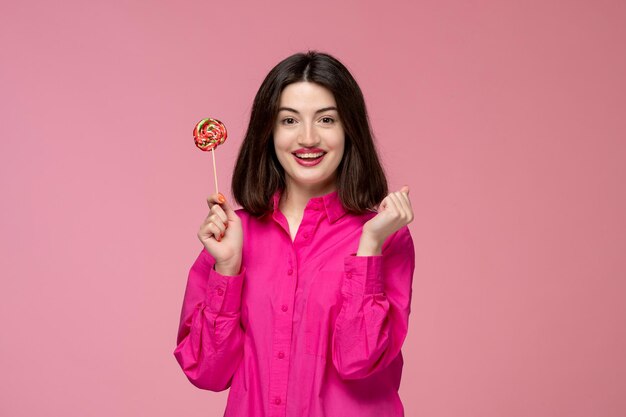Nettes Mädchen hübsches junges schönes Brunettemädchen im rosafarbenen Hemd glücklich mit einem runden Lutscher