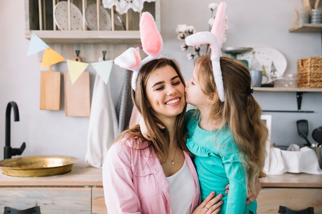 Nettes Mädchen in den Häschenohren Mutter auf Backe küssend