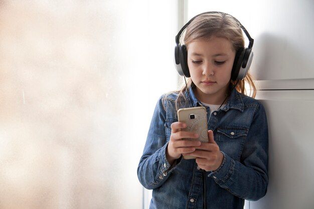 Nettes Mädchen in den Kopfhörern, die Smartphone verwenden