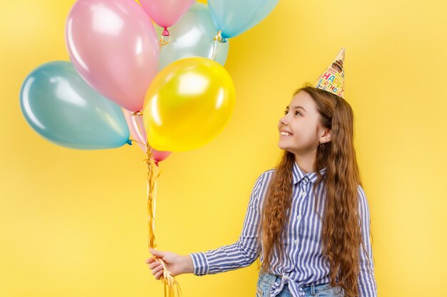 Nettes Mädchen in Geburtstagsfeier mit bunten aufblasbaren Ballons isoliert auf einer gelben Wand