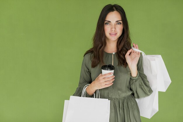 Nettes Mädchen mit Kaffee und vielen Einkaufsnetzen auf grünem Hintergrund