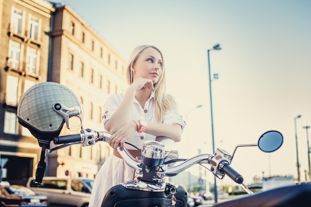 Kostenloses Foto nettes mädchen mit langen blonden haaren in weißem kleid mit roller auf einer stadtstraße